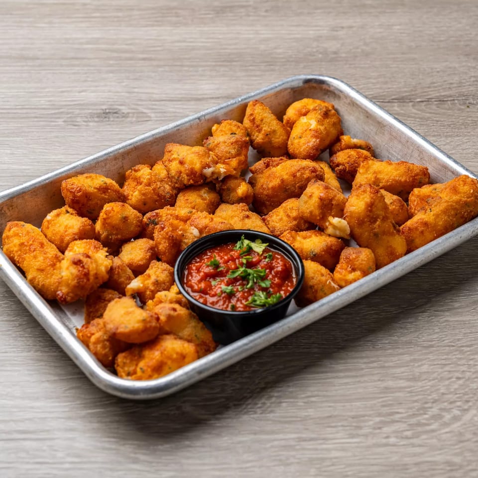 Crispy fried cheese curds with a side of marinara sauce on a metal tray at Dempsey Burger Bar.