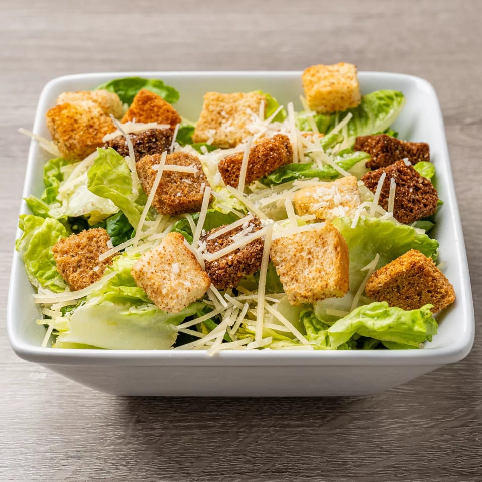 Caesar salad in a white bowl with green lettuce, croutons, and shredded cheese.