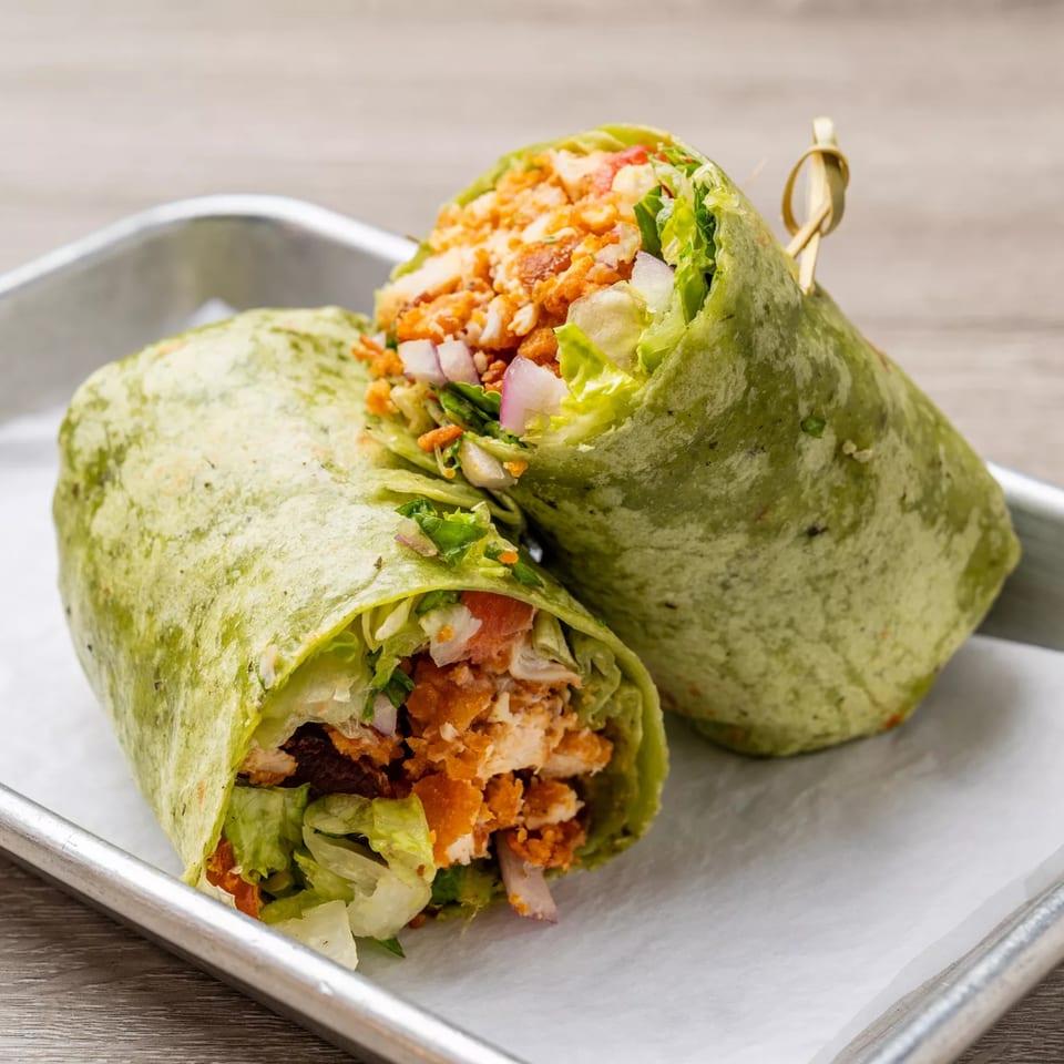 Two halves of a green tortilla wrap filled with buffalo chicken, lettuce, and red onion.
