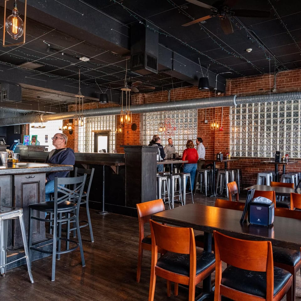 Dempsey Burger Bar interior with brick walls, glass block windows, and patrons at tables and bar.