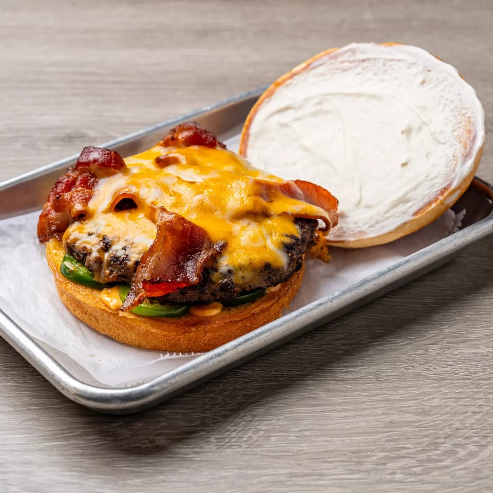 Dempsey Burger Bar's bacon cheeseburger with jalapeños and a creamy bun on a metal tray.