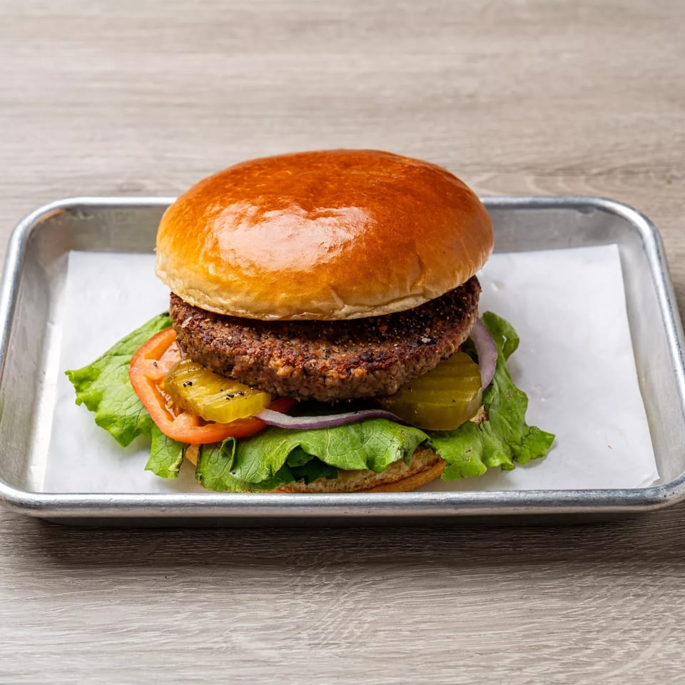 Dempsey Burger Bar's burger with lettuce, tomato, onion, and pickles on a metal tray.