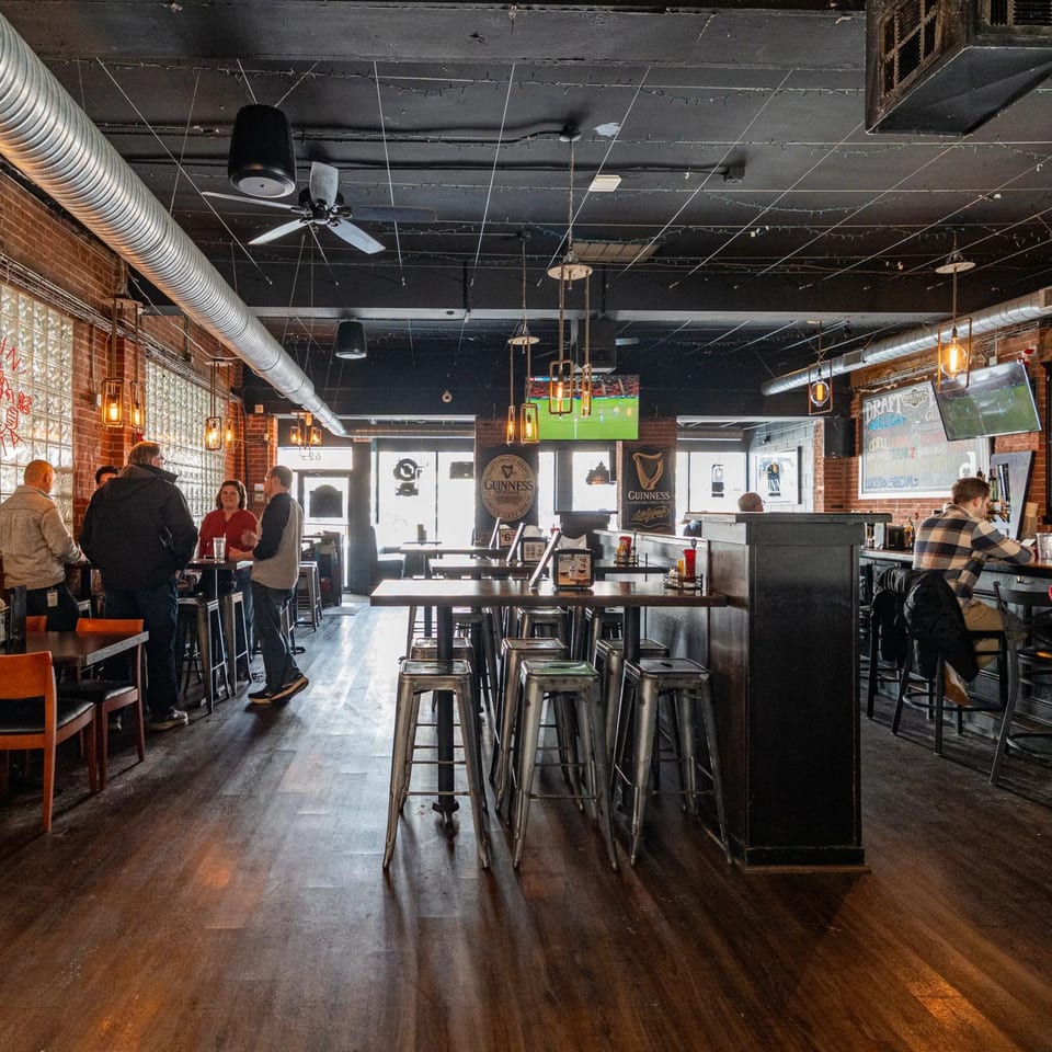 Dempsey Burger Bar's interior with patrons, high-top tables, a bar, and exposed brick walls.