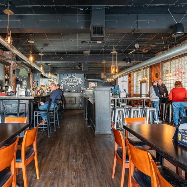 Interior of DEMPSEY BURGER BAR with patrons at the bar and high-top tables, featuring industrial decor.