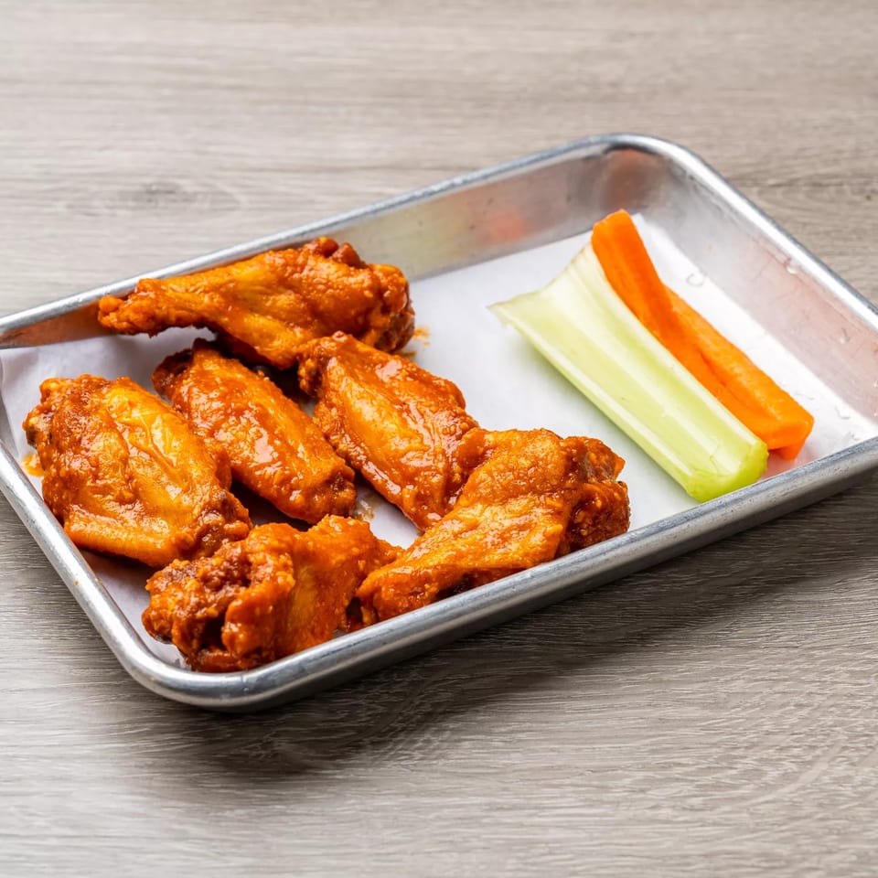 Dempsey Burger Bar's buffalo wings with celery and carrot sticks on a metal tray.