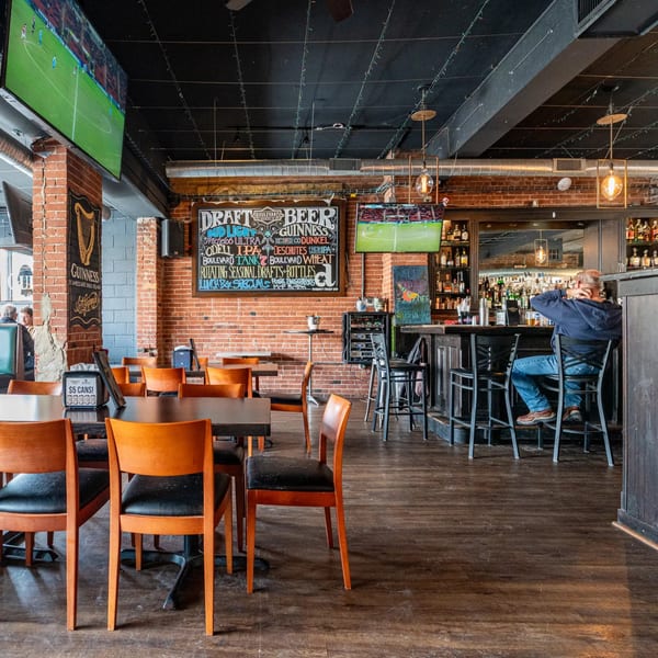 Interior of Dempsey Burger Bar with a man at the bar, tables, and TVs showing sports.