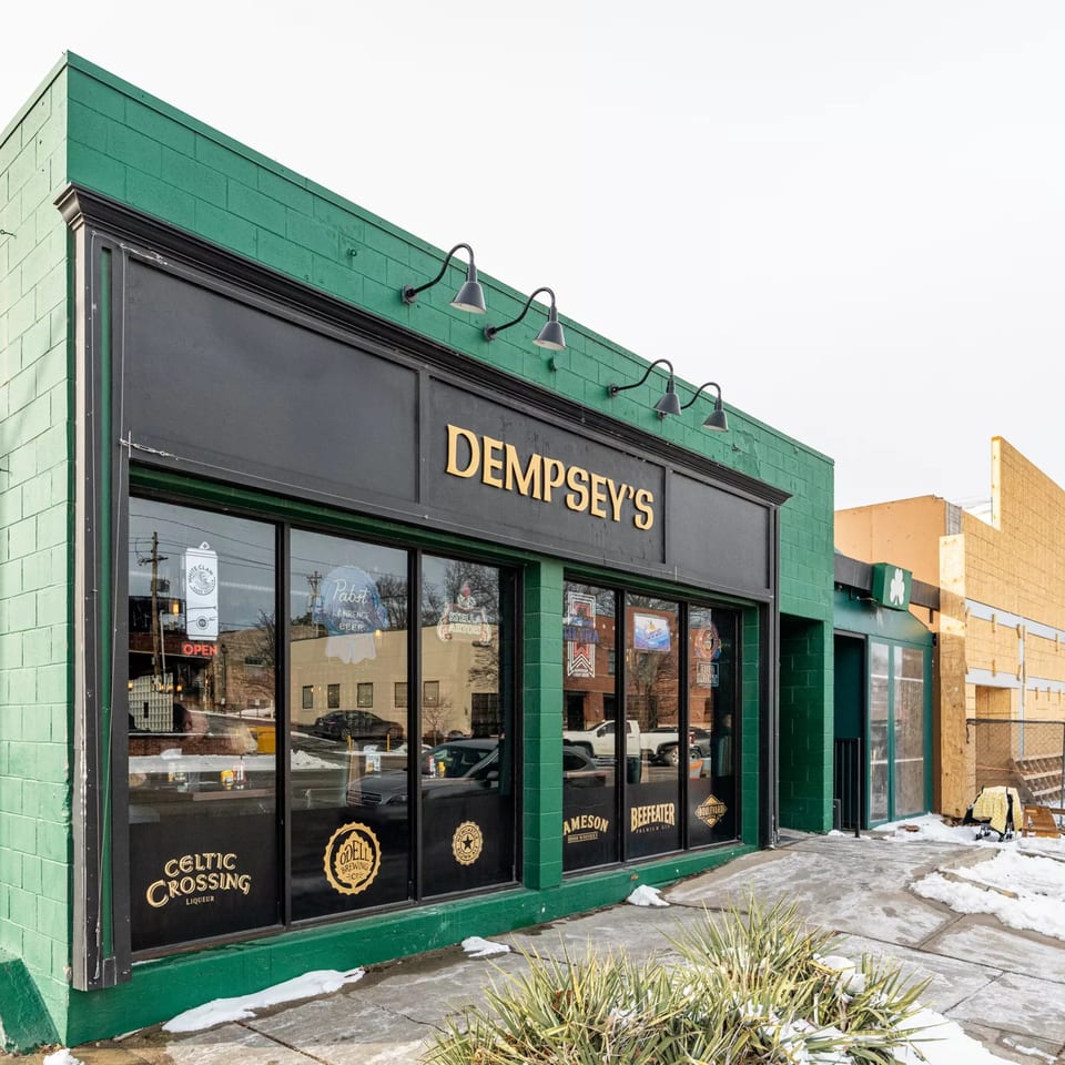 Exterior of Dempsey's bar-&-grill, a green brick building with large windows and golden signage.