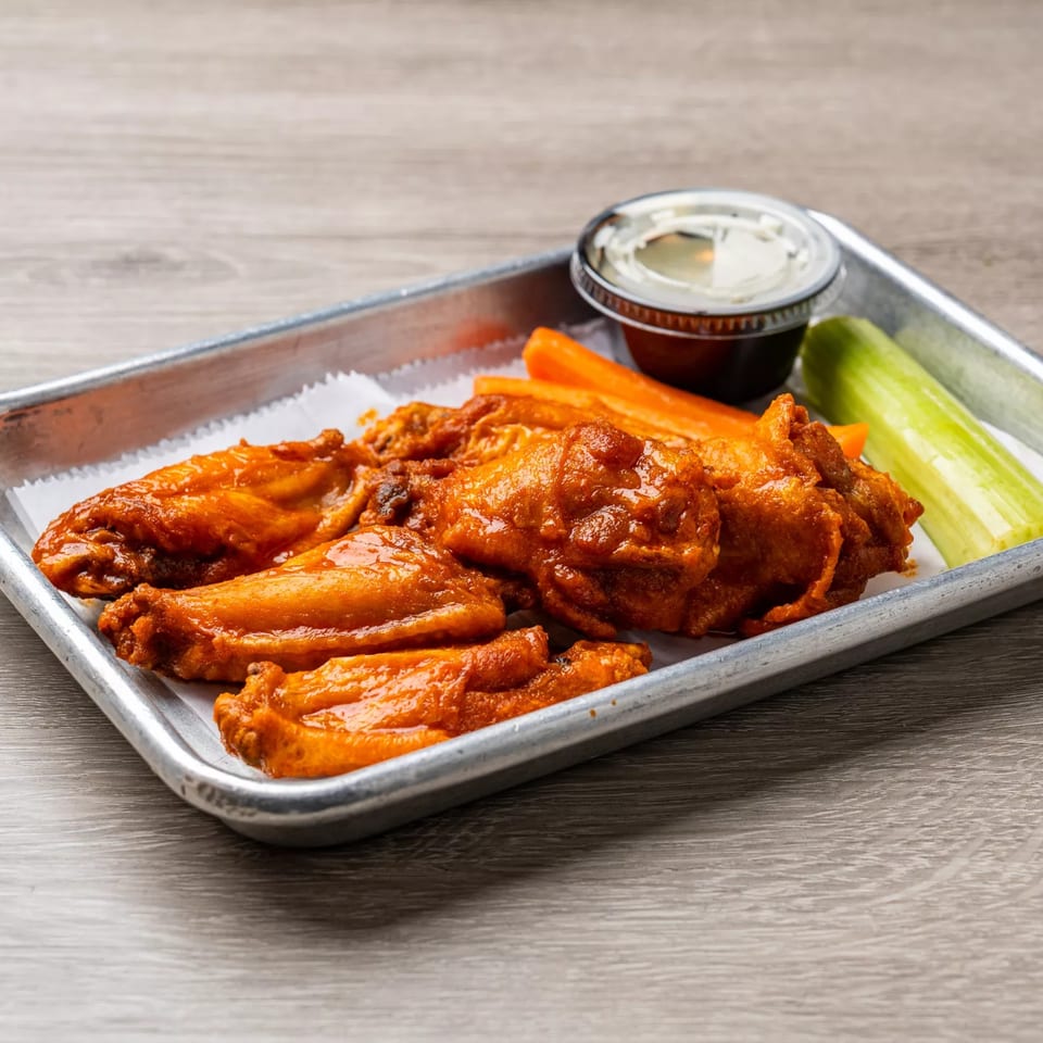 Spicy Dempsey Burger Bar chicken wings with celery, carrots, and dipping sauce on a metal tray.