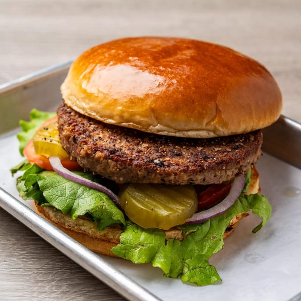 A DEMPSEY BURGER BAR burger with a thick patty, lettuce, tomato, onion, and pickles on a bun.
